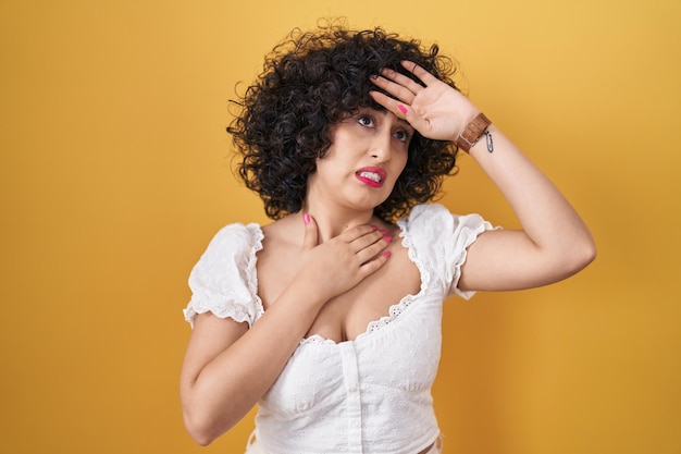 Photo gratuite jeune femme brune aux cheveux bouclés debout sur fond jaune touchant le front pour la maladie et la fièvre, la grippe et le rhume, le virus malade