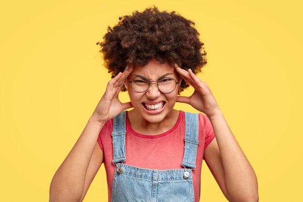 Jeune femme brune aux cheveux bouclés et salopette en denim