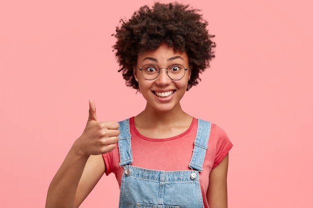 Jeune femme brune aux cheveux bouclés et salopette en denim