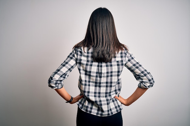 Photo gratuite jeune femme brune aux yeux bleus portant une chemise décontractée et des lunettes sur fond blanc debout en arrière regardant loin avec les bras sur le corps