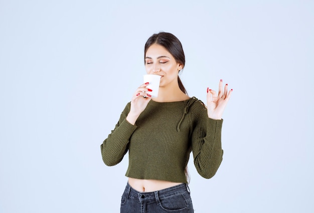 Jeune femme brune buvant une tasse de thé en plastique et donnant un signe ok.