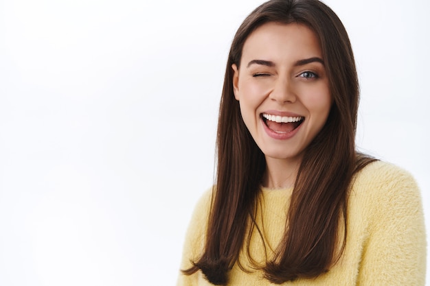 Photo gratuite jeune femme brune effrontée et insouciante en pull jaune, caméra clin d'œil coquette et souriante, assure que tout est génial, encourage à profiter d'une belle journée de printemps