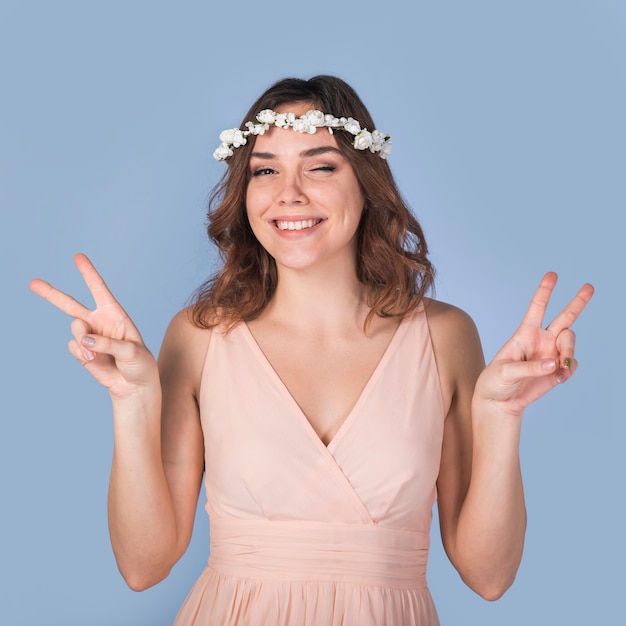 Photo gratuite jeune femme brune joyeuse avec une couronne de belle fleur montrant le geste de la paix