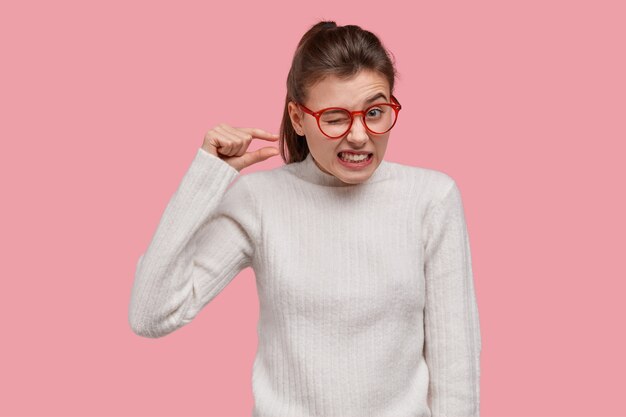 Jeune femme brune portant un pull blanc et des lunettes rouges