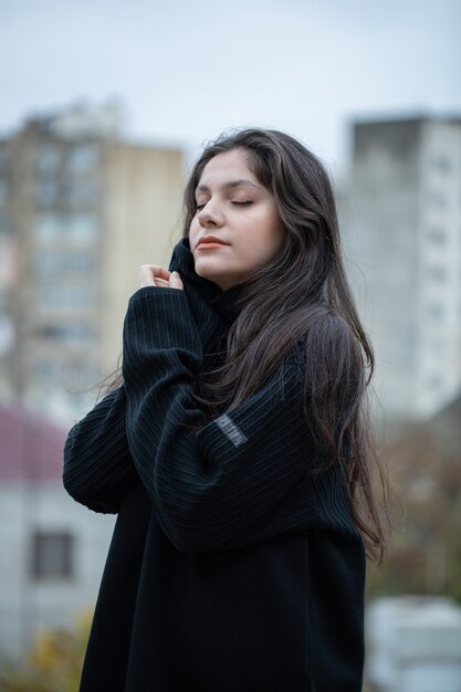 Jeune femme brune en pull noir debout en plein air