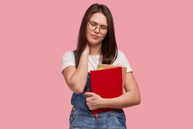 Jeune femme brune en salopette en denim tenant des blocs-notes