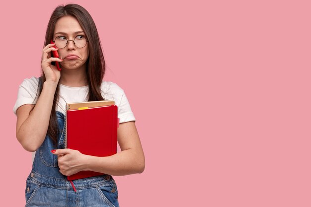 Jeune femme brune en salopette en denim tenant des blocs-notes