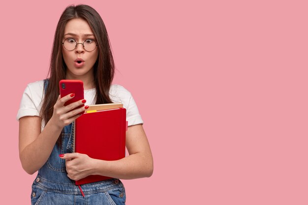 Jeune femme brune en salopette en denim tenant des blocs-notes