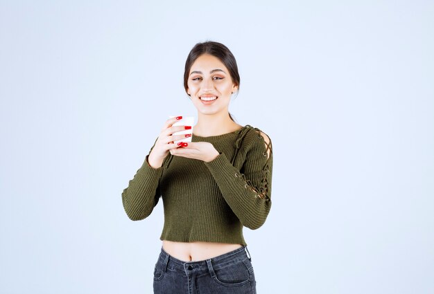 Jeune femme brune tenant une tasse en plastique avec bonheur sur fond blanc.