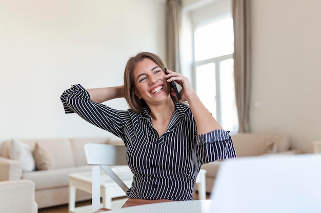 Jeune femme de bureau parlant à quelqu'un sur son téléphone portable tout en regardant au loin avec une expression faciale heureuse