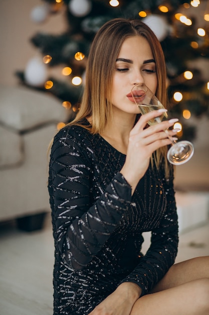 Jeune femme buvant du champagne par arbre de Noël