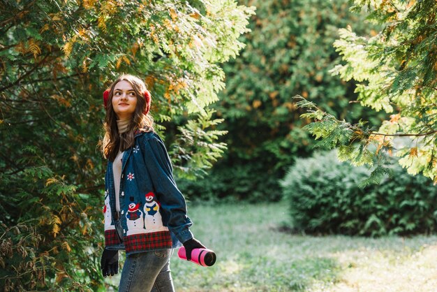 Jeune femme, cache-oreilles, tenue, thermos, près, brindilles vertes