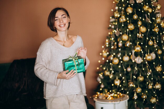 Jeune femme avec un cadeau de Noël près du sapin de Noël