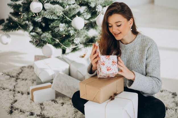 Jeune femme avec des cadeaux de Noël par l'arbre de Noël