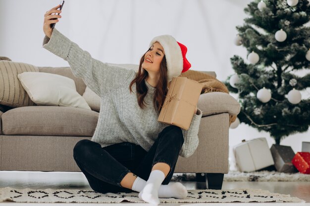 Jeune femme avec des cadeaux de Noël par l'arbre de Noël