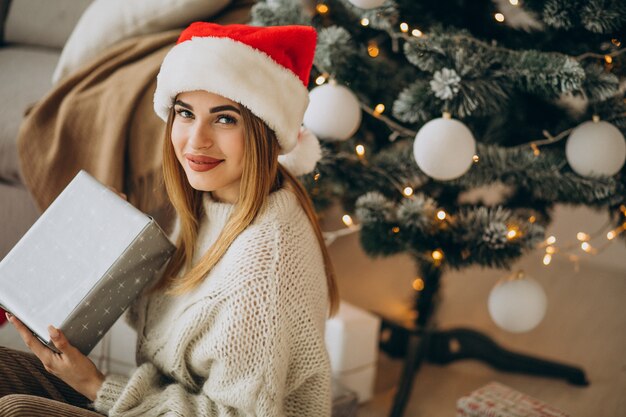 Jeune femme avec des cadeaux de Noël par l'arbre de Noël