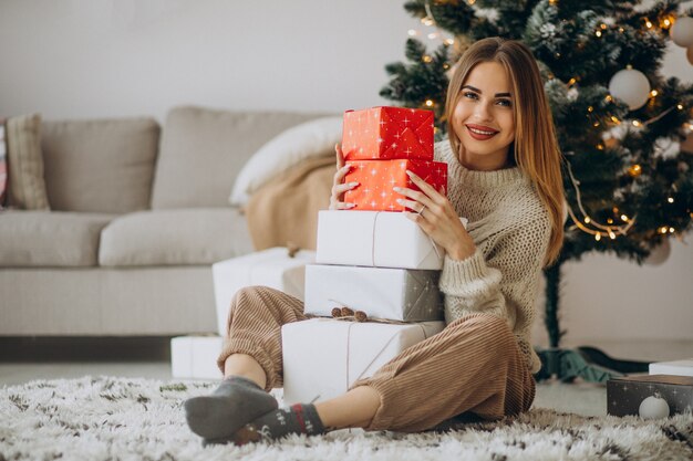 Jeune femme avec des cadeaux de Noël par l'arbre de Noël