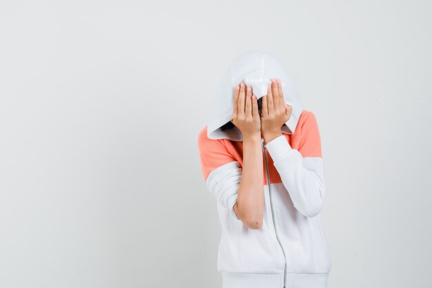 Jeune femme à capuche couvrant le visage avec ses mains et à la malheureuse