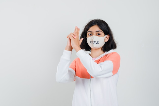 Jeune femme à capuche, masque facial montrant le geste du pistolet et à l'attention