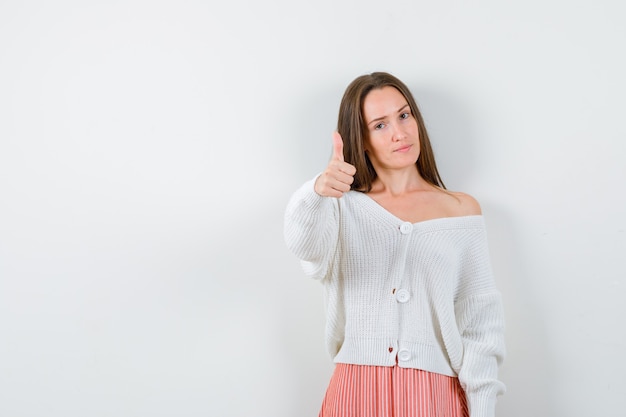 Jeune femme en cardigan et jupe montrant le pouce vers le haut à la confiance isolée