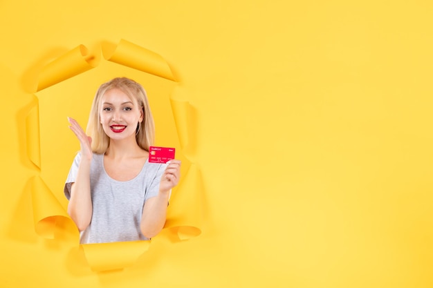 Jeune femme avec carte de crédit sur fond de papier jaune déchiré money bank shopping