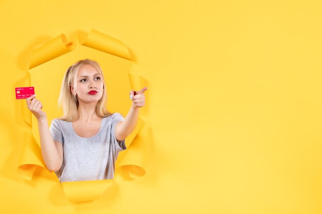 Jeune femme avec carte de crédit pointant sur quelque chose sur une surface de papier jaune déchiré