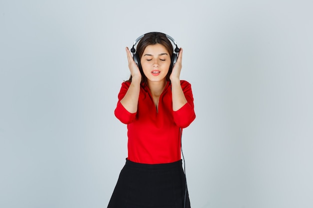 Jeune femme avec un casque d'écoute de la musique en chemisier rouge, jupe et à ravi