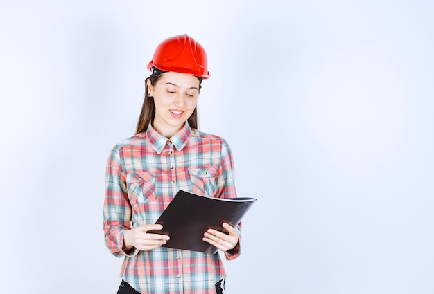 Une jeune femme en casque de protection prenant des notes dans un dossier noir .