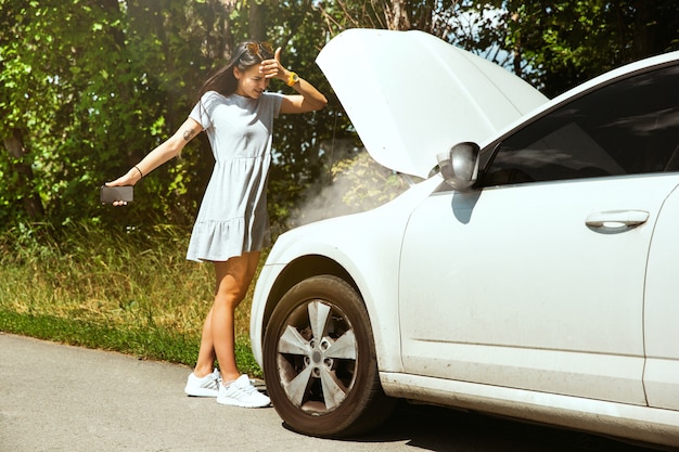 Photo gratuite la jeune femme a cassé la voiture alors qu'elle voyageait pour se reposer. elle essaie de réparer elle-même les bris ou devrait faire du stop. devenir nerveux