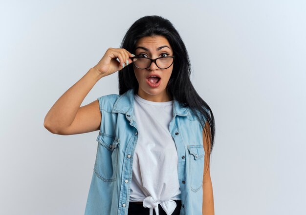 Une jeune femme caucasienne choquée tient et regarde à travers des lunettes optiques