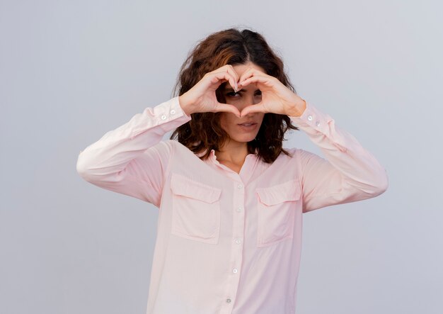 Une jeune femme caucasienne confiante fait des gestes et regarde à travers le signe de la main du coeur