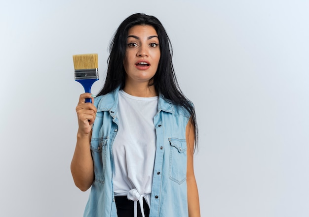 La jeune femme caucasienne étonnée tient la brosse de peinture