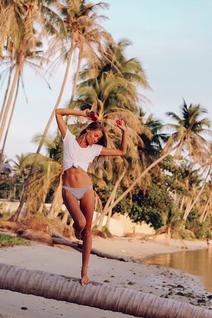 Jeune femme caucasienne fit avec pastèque sur la plage tropicale au coucher du soleil. Sport à la femme en haut blanc et culotte ayant des fruits tropicaux