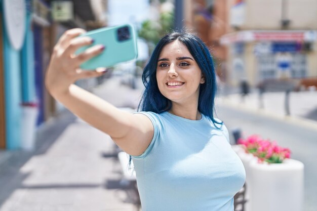 Une jeune femme caucasienne souriante et confiante se fait un selfie avec son smartphone dans la rue.