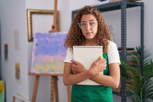 Jeune femme caucasienne tenant un cahier d'art sceptique et nerveux fronçant les sourcils contrarié à cause d'un problème de personne négative