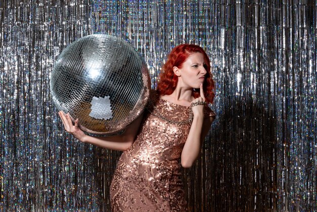 Jeune femme célébrant le nouvel an en fête tenant une boule disco sur des rideaux lumineux rideaux