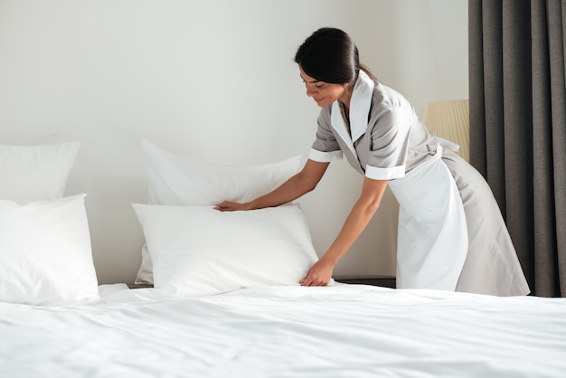 Jeune femme de chambre d'hôtel mise en place d'oreiller sur le lit