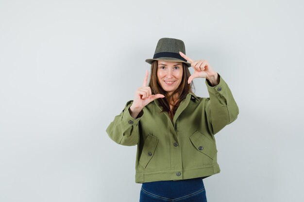 Jeune femme en chapeau de pantalon de veste faisant le geste du cadre et à la joyeuse