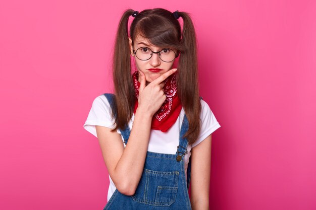 Jeune femme charismatique enfantine met la main sur le visage, réfléchit à ses plans, fait la grimace