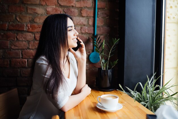 Jeune femme charmante appelant avec téléphone portable alors qu'il était assis seul dans un café