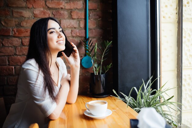 Jeune femme charmante appelant avec téléphone portable alors qu'il était assis seul dans un café