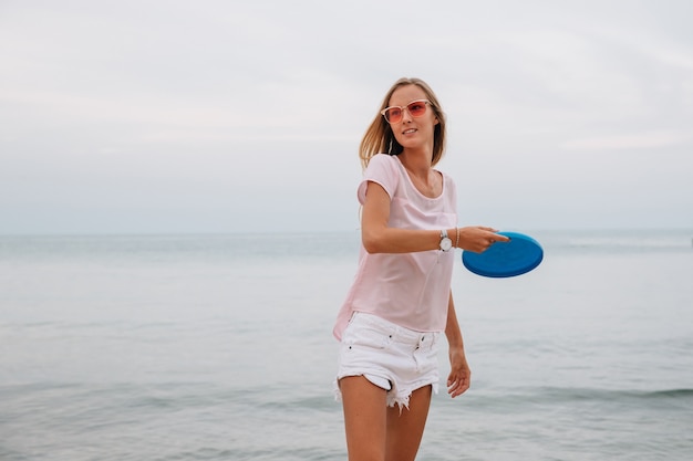 Jeune femme charmante jouant au frisbee près de la mer, tenant le disque de frisbee.