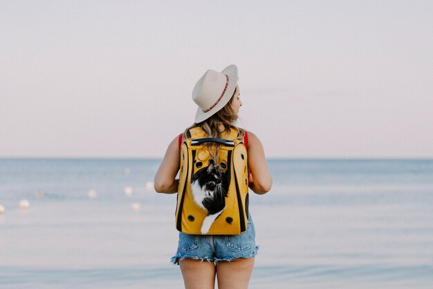 jeune femme avec un chat dans un sac à dos au bord de la mer. Concept de voyage avec un animal de compagnie. Chat dans le sac à dos avec hublot.