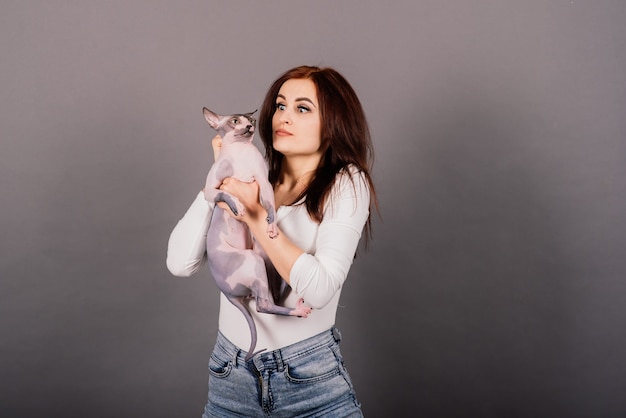 Jeune femme avec chat sphynx canadien en studio, fond gris