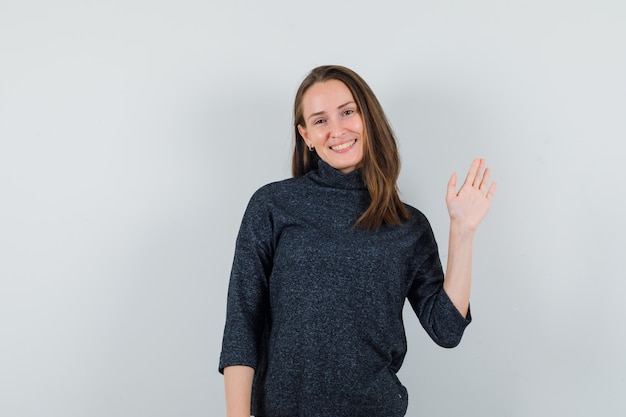 Jeune femme en chemise en agitant la main pour dire au revoir et à la joyeuse