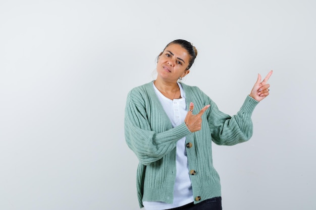 Photo gratuite jeune femme en chemise blanche et cardigan vert menthe pointant vers la droite avec l'index et à la grave