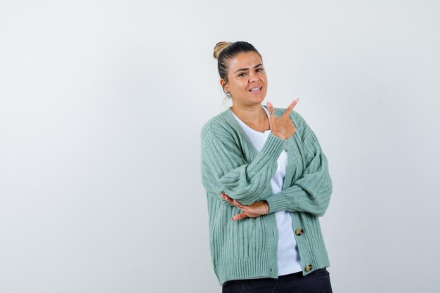 Jeune femme en chemise blanche et cardigan vert menthe pointant vers le haut et à heureux