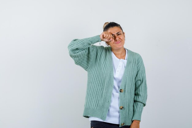 Jeune femme en chemise blanche et cardigan vert menthe se frottant les yeux et ayant l'air fatigué