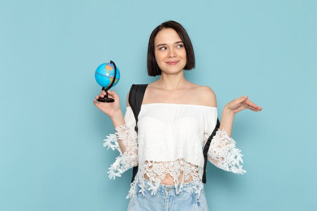 jeune femme en chemise blanche et sac noir tenant petit globe sur bleu