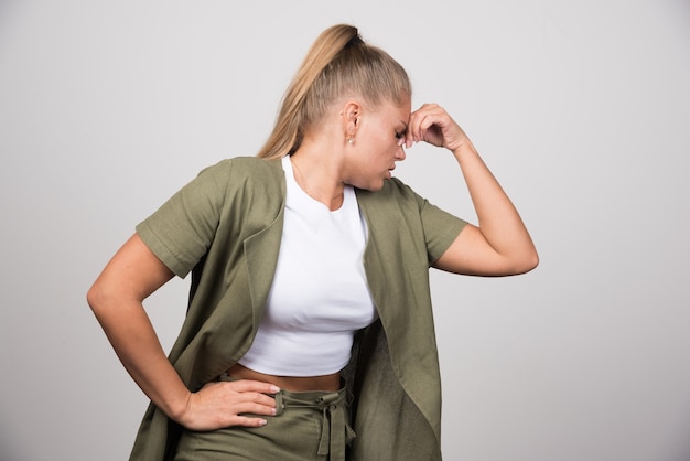 Jeune femme en chemise blanche se sentant douloureuse sur un mur gris.